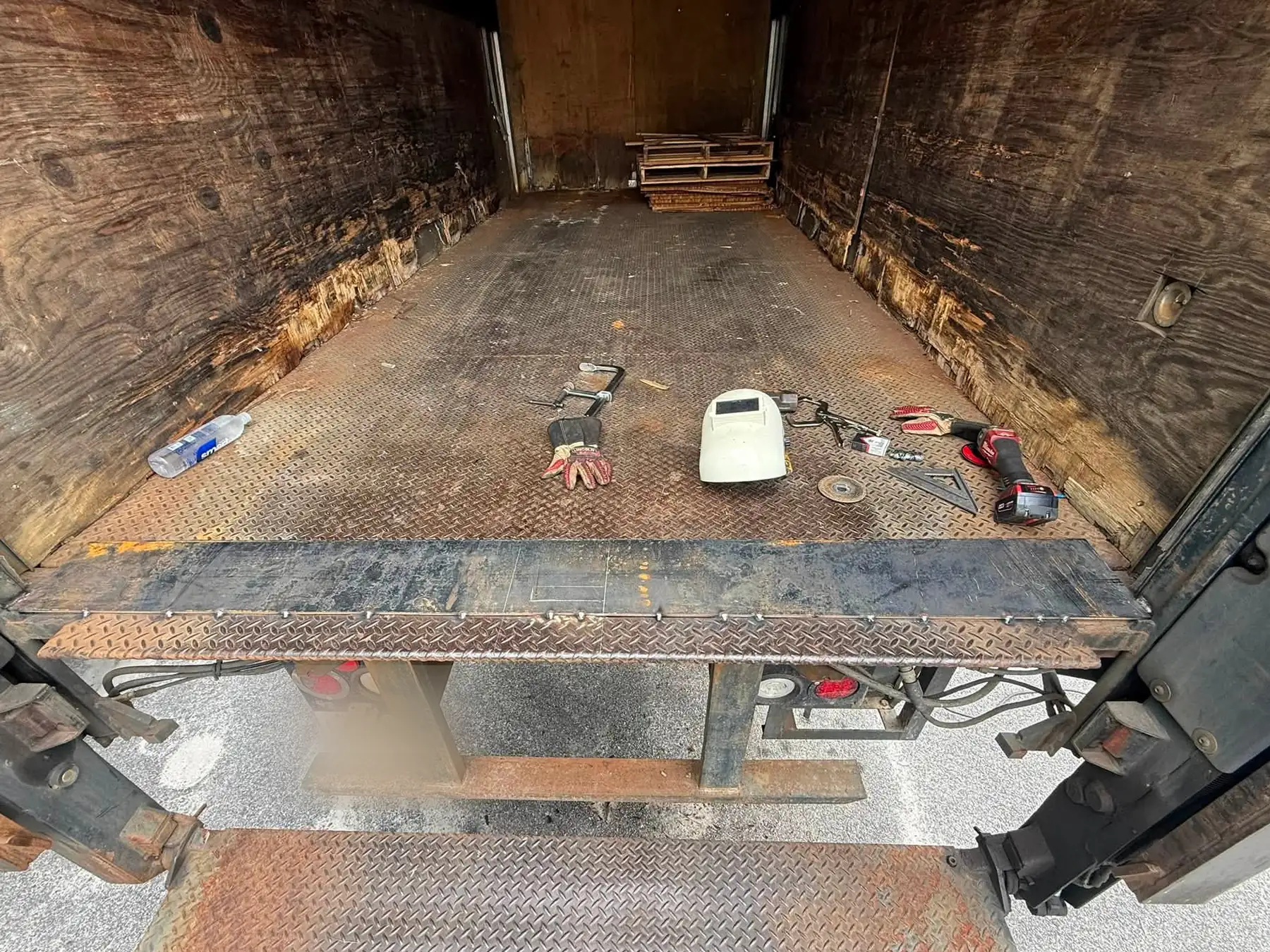 Rusted and worn threshold plate at the rear of a box truck before repair, tools staged on the floor