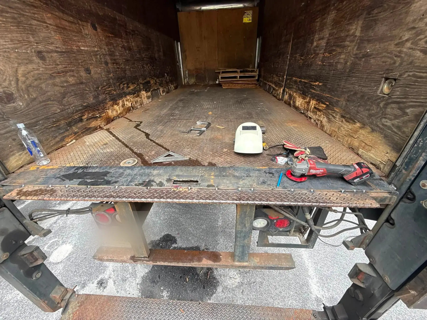 Inside a box truck before repair, with rotted plywood side walls and a worn diamond plate floor