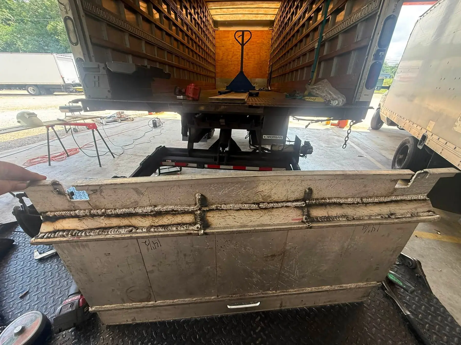 Rebuilt liftgate platform held up beside a box truck in a customer's fleet yard, with more trucks parked behind