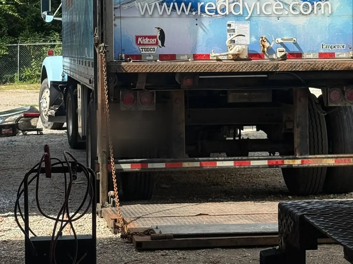 A box truck with its rear open during an on-site liftgate repair, welding gear standing on the gravel beside it