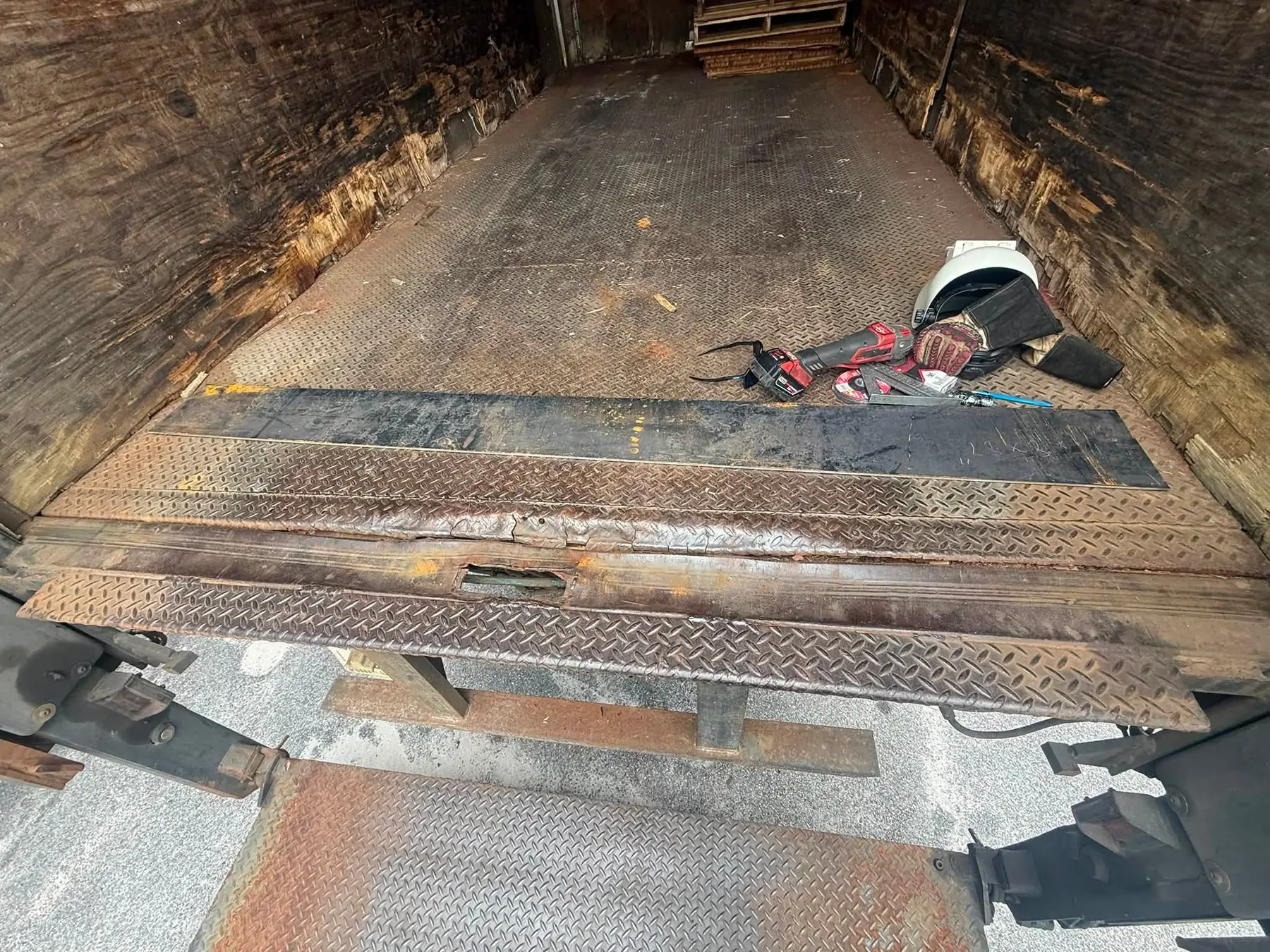 Worn rusted threshold plate inside a box truck with a saw, gloves and hard hat staged on the floor