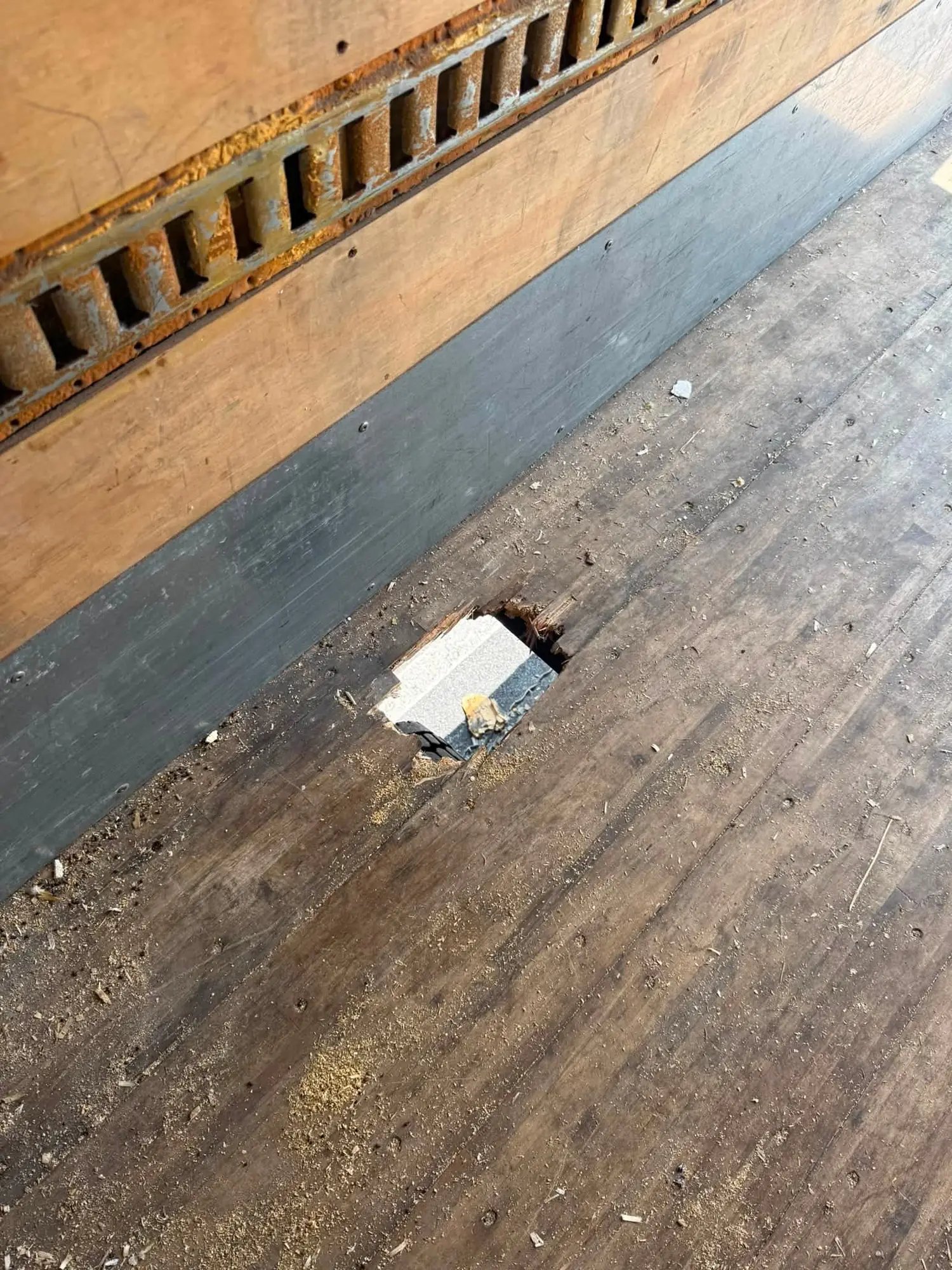 A hole rotted through the hardwood floor of a box truck with fresh sawdust around it